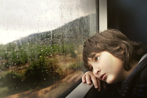 窓の外を見ながら雨で憂鬱な女性