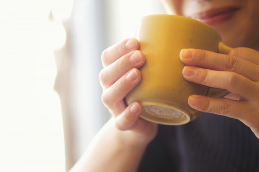 マグカップで温かい飲み物を飲んでいる手元